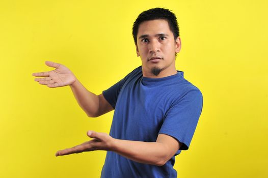 Young man asking questions with hands raised, isolated on yellow background