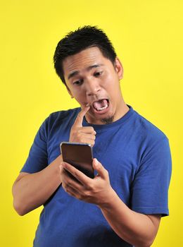 Funny Asian man using cellphone, isolated on yellow background