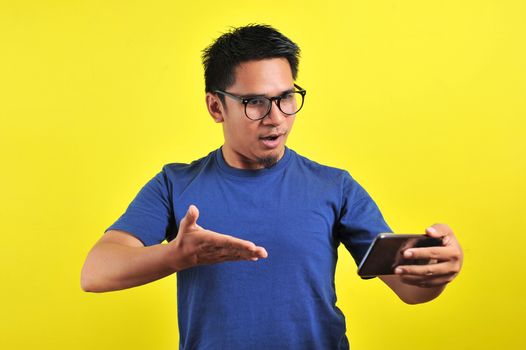 Asian man shocked what he see in the smartphone, isolated on yellow background
