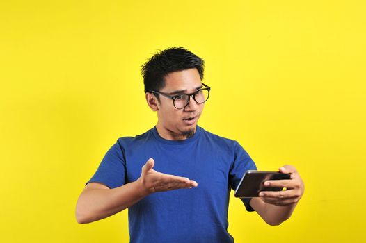 Asian man shocked what he see in the smartphone, isolated on yellow background