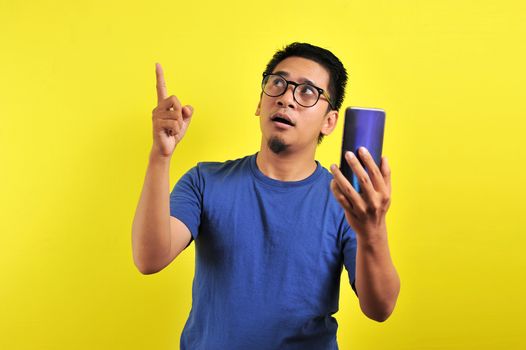 Happy young Asian man smiling using smartphone looking at blank area, isolated on yellow background