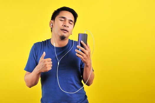 Portrait of Asian man listening of music from smartphone with closed eyes, isolated on yellow background