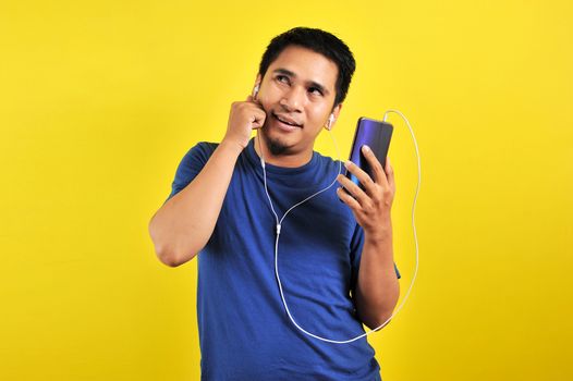 Asian man listening of music from smartphone looking at copy space, isolated on yellow background
