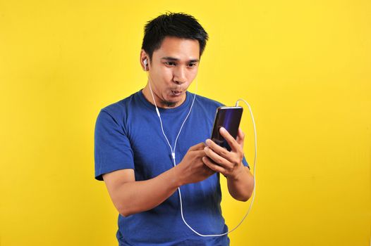 Portrait of excited Asian man surprised to find a trending song on online, isolated on yellow background