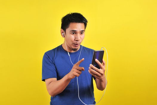 Portrait of excited Asian man surprised to find a trending song on online, isolated on yellow background