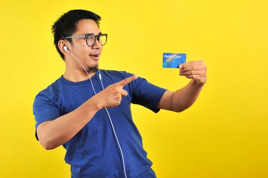 Young Asian man love his debit card, isolated on yellow background 