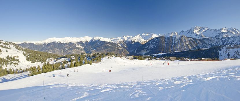 Panoramic view over a piste at ski resort with mountains in background