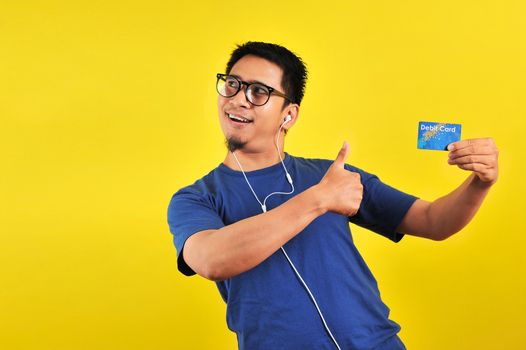 Young Asian man love his debit card, isolated on yellow background 