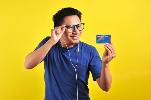 Young Asian man love his debit card, isolated on yellow background 