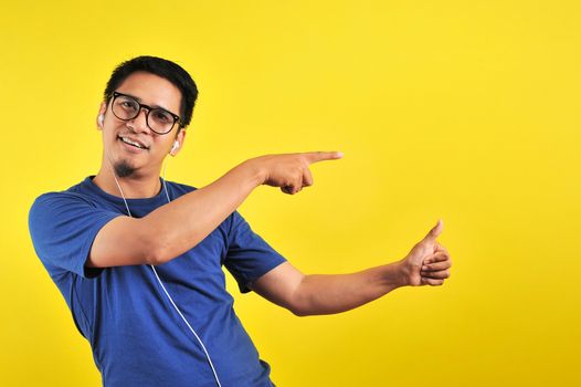 Handsome of happy smiling asian man pointing of a copyspace, isolated on yellow background