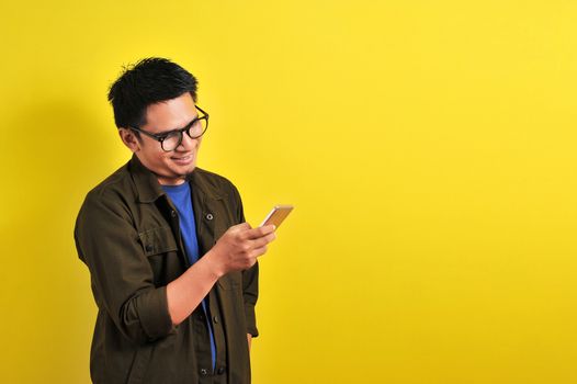 Portrait of happy smiling Asian man using smartphone wearing casual t-shirt and jacket with eyesglasses, get the best price, using simple mobile banking payment