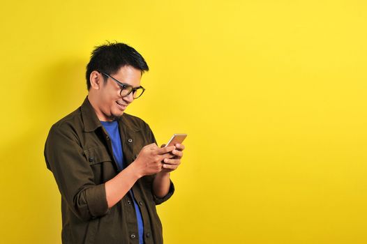 Portrait of happy smiling Asian man using smartphone wearing casual t-shirt and jacket with eyesglasses, get the best price, using simple mobile banking payment