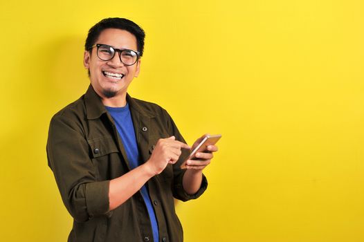 Portrait of happy smiling Asian man using smartphone wearing casual t-shirt and jacket with eyesglasses, get the best price, using simple mobile banking payment