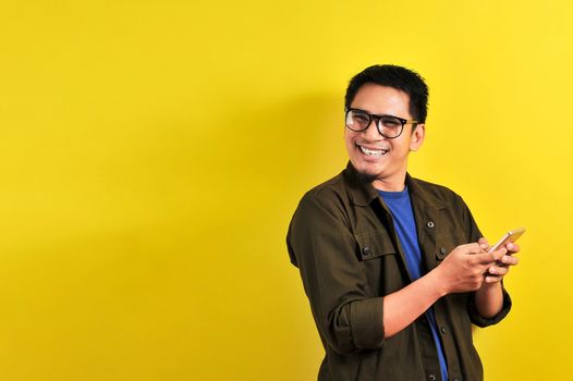 Portrait of happy smiling Asian man using smartphone wearing casual t-shirt and jacket with eyesglasses, get the best price, using simple mobile banking payment