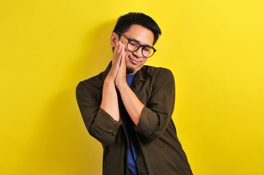 Asian man wear eyeglasses with sleep gesture, isolated on yellow