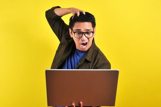 Asian online freelancer very angry in front of his laptop, get bad report from customer, isolated on yellow