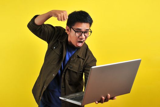 Asian online freelancer very angry in front of his laptop, get bad report from customer, isolated on yellow