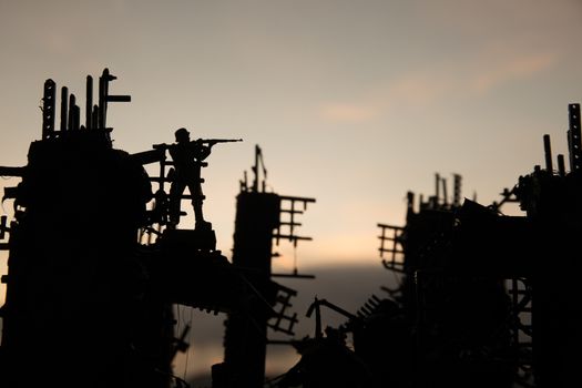 Army sniper with large caliber rifle standing in the fire and smoke. War Concept. Battle scene on war fog sky background, Fighting silhouettes Below Cloudy Skyline at sunset. City destroyed by war