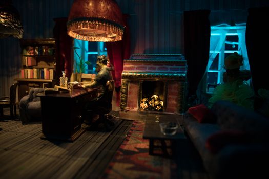 A realistic dollhouse living room with furniture and window at night. Man sitting on table in dark room. Selective focus.