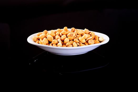 Roasted Salted Peanuts in a white plate on a black background