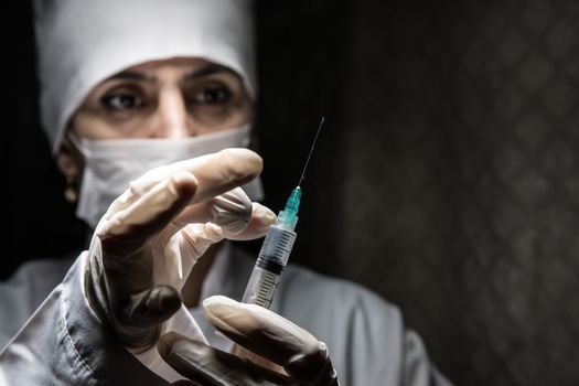 Health medical concept. Serious female doctor in medical mask holding syringe. Health worker dials the vaccine into a syringe on dark background.