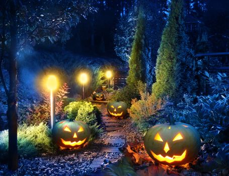 Dark home garden illuminated patio lights with halloween pumpkin lanterns along the path
