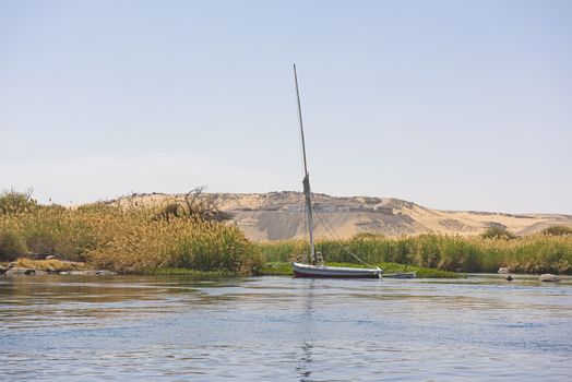 Sailing down large wide river Nile in Aswan Egypt through rural countryside landscape with rocky cataract islands and mountain background