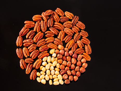 Assorted nuts (Pecan, Hazelnuts and Roasted Salted Peanuts) in a circle form on a black background