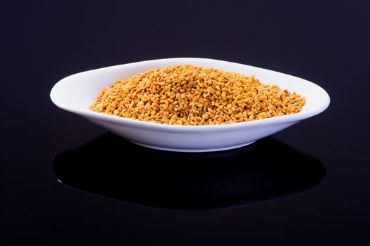 Fenugreek seeds in a white bowl on black surface