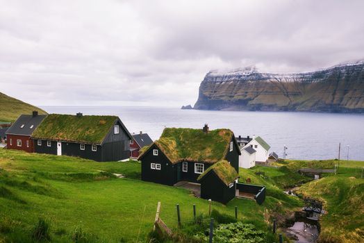Village of Mikladalur located on the island of Kalsoy in Faroe Islands with snow-capped mountains in the background