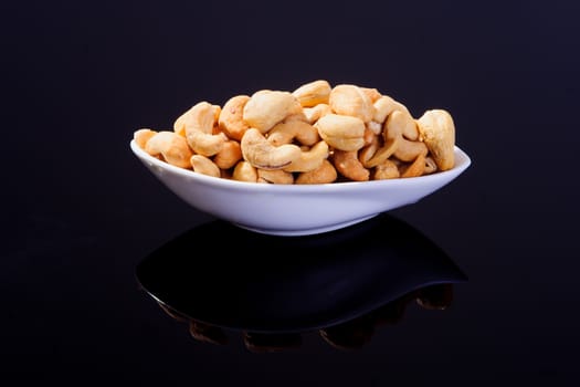 Salted Cashew Nuts in a white plate on a black background