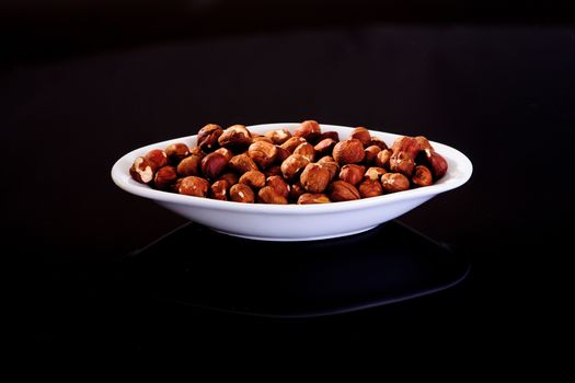 Hazelnuts in a white plate on a black background