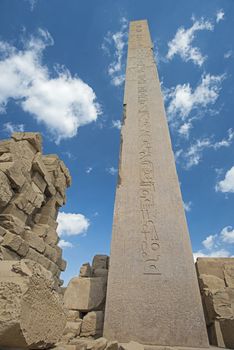 Large tall ancient egyptian obelisk at the temple of Karnak in Luxor with hieroglyphic carvings on blue sky background