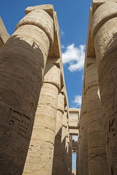 Columns with hieroglyphic carvings in hypostyle hall at anciant egyptian Karnak Temple in Luxor with blue sky background
