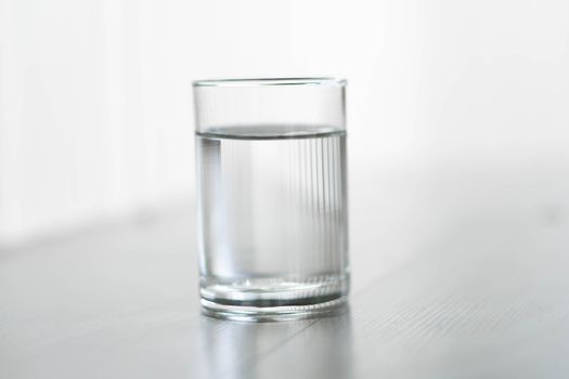 Glass of water on wood table with light in the morning, healthy care concept, selective focus