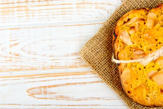 Fresh bakery. Top view of baked pie with apples on sackcloth on a white wooden background. Rustic style.