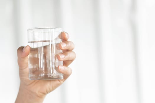 Closeup woman hand holding a glass of pure water for dink with grey background, Health care concept