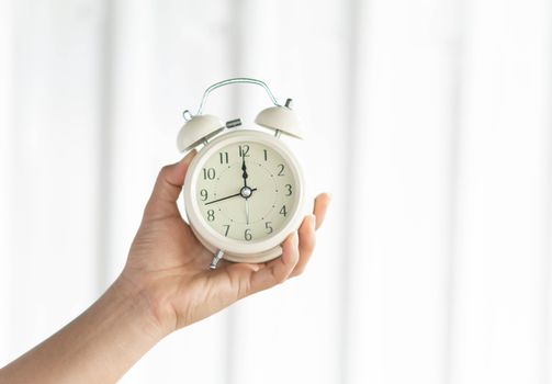 Closeup hand holding alarm clock on white background, Time to wake up