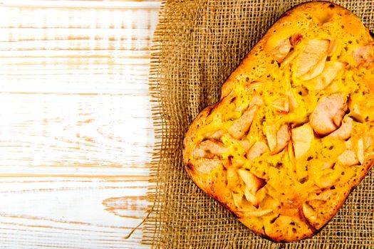 Fresh bakery. Top view of baked pie with apples on sackcloth on a white wooden background. Rustic style.