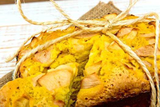 Fresh bakery. Close-up of baked pie with apples on sackcloth on a white wooden background. Rustic style.