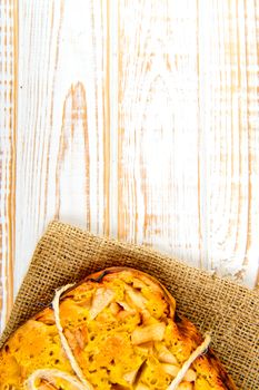 Fresh bakery. Top view of baked pie with apples on sackcloth on a white wooden background. Rustic style.
