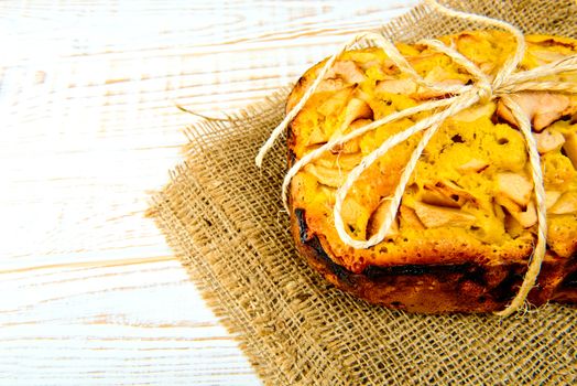 Fresh bakery. Baked pie with apples on sackcloth on a white wooden background. Rustic style.