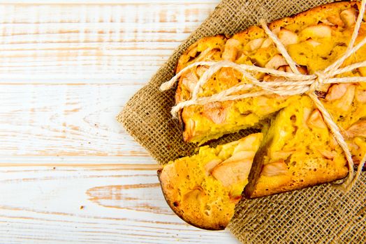 Fresh bakery. Top view of baked pie with apples on sackcloth on a white wooden background. Rustic style.