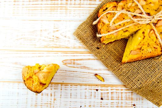 Fresh bakery. Top view of baked pie with apples on sackcloth on a white wooden background. Rustic style.