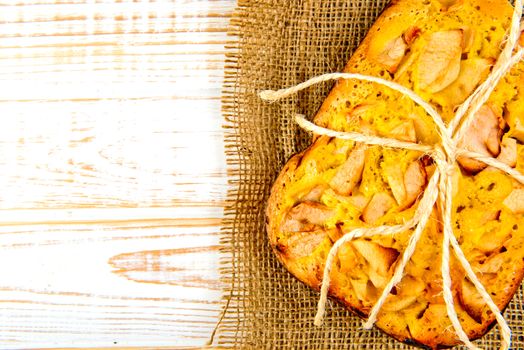 Fresh bakery. Top view of baked pie with apples on sackcloth on a white wooden background. Rustic style.