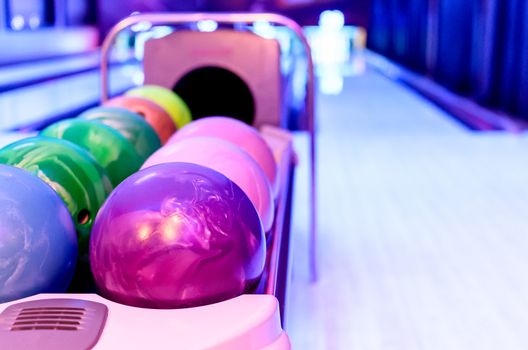 A Purple Bowling balls has ready for player to throwing ball on the wooden lane and in the bowling hall.