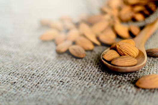 A lot of almonds has putting on the wood spoon and brown napkin.