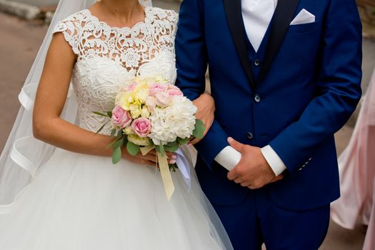 The bride and groom stand with their hands together. The bride's bouquet.