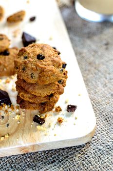 Chocolate Chip Cookies on wood block and brown linen napkin on wooden table and drinking with coffee in the dessert time.