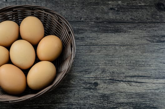 Chicken eggs in brown basket on brown wooden table background.